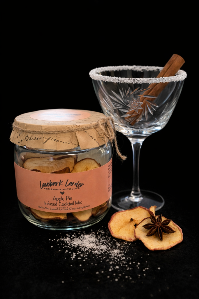 Jar of Apple Pie Infused Cocktail Mix with a glass and cinnamon stick on a dark background